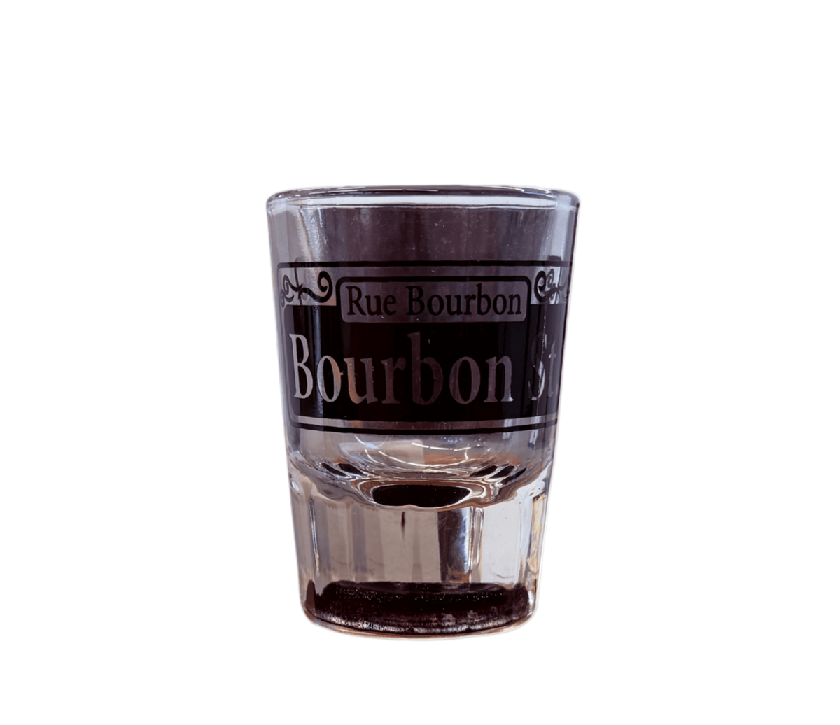 A clear glass shot glass featuring a black printed label with the text 'Rue Bourbon' and 'Bourbon St' in white lettering, set against a plain white background.