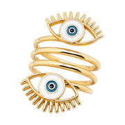A gold-plated spiral ring featuring two evil eye charms with white enamel, blue and black detailing, and gold eyelashes, set against a plain white background.