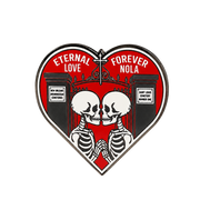 A heart-shaped enamel pin featuring two skeletons kissing in front of a red gothic gate, with white text reading 'ETERNAL LOVE FOREVER NOLA' and cemetery sign details on a white background.