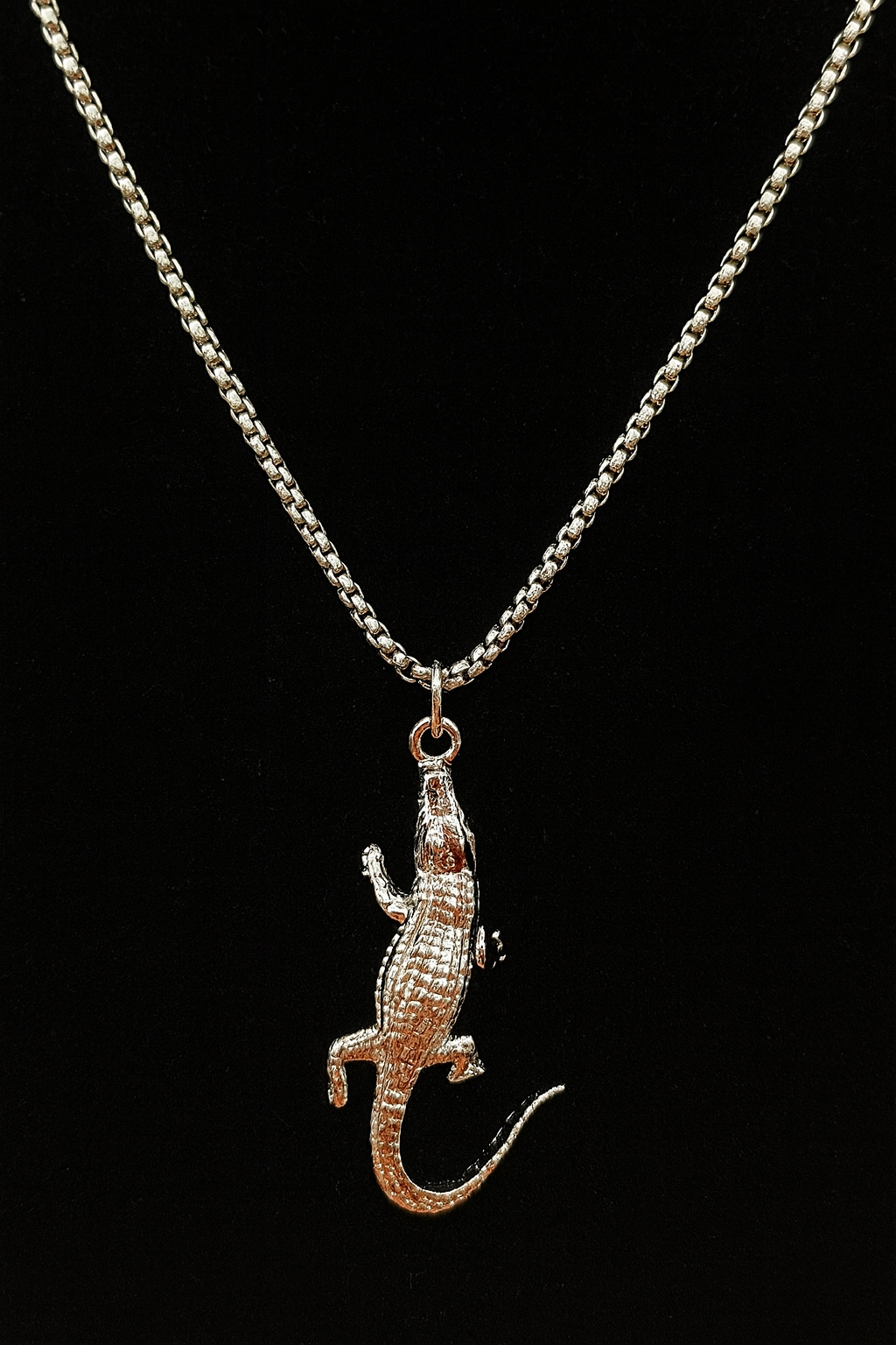 Rose gold alligator pendant on a silver chain against a black background