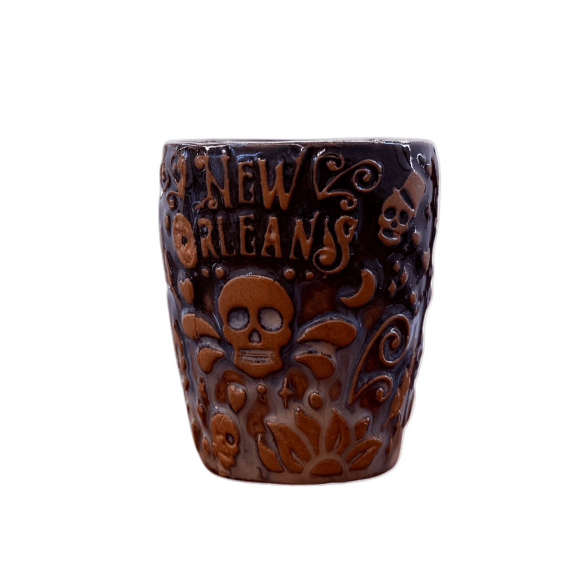 A dark brown ceramic shot glass featuring embossed New Orleans-themed designs, including a central skull and the words 'NEW ORLEANS' in raised lettering, set against a plain white background.