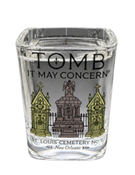 A clear glass shot glass featuring a black and white illustration of a cemetery monument with two green-tinted tombstones, and the text 'TOMB IT MAY CONCERN' and 'ST. LOUIS CEMETERY NO.